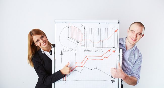 Successful business partners standing by whiteboard with graph of market analysis on it